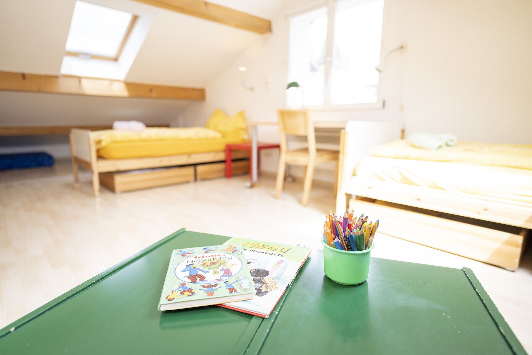 A child's room with bunk beds, a desk, and a green table with a book and colored pencils.