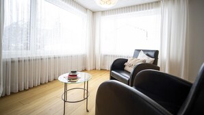 Ein Zimmer mit einem großen Fenster, einem schwarzen Ledersofa, einem Glastisch und einer Pendelleuchte.