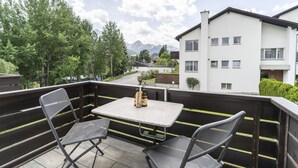 A balcony with two chairs and a table, overlooking a residential area with a mountain in the background. - Chasa Trü No. 8: Idyllic 2.5-room flat in the Trü holiday village (Scuol)