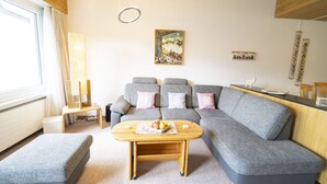 A modern living room with a grey sectional sofa, a wooden coffee table, and a painting on the wall. - Chasa Trü No. 8: Idyllic 2.5-room flat in the Trü holiday village (Scuol)