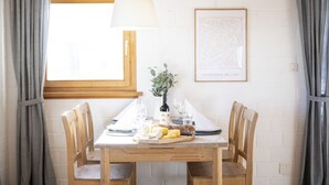 A dining table set with plates, glasses, and a bottle of wine, surrounded by wooden chairs. - Chasa Fabulusa: Modern 2.5-room apartment in the centre of Ftan (Ftan)
