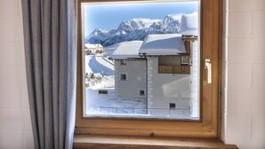 A window with a view of a mountain range and a building with a snow-covered roof. - Chasa Fabulusa: Modern 2.5-room apartment in the centre of Ftan (Ftan)