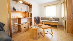 Un salon chaleureux avec un plancher en bois, un canapé, un fauteuil, une petite table et une bibliothèque.