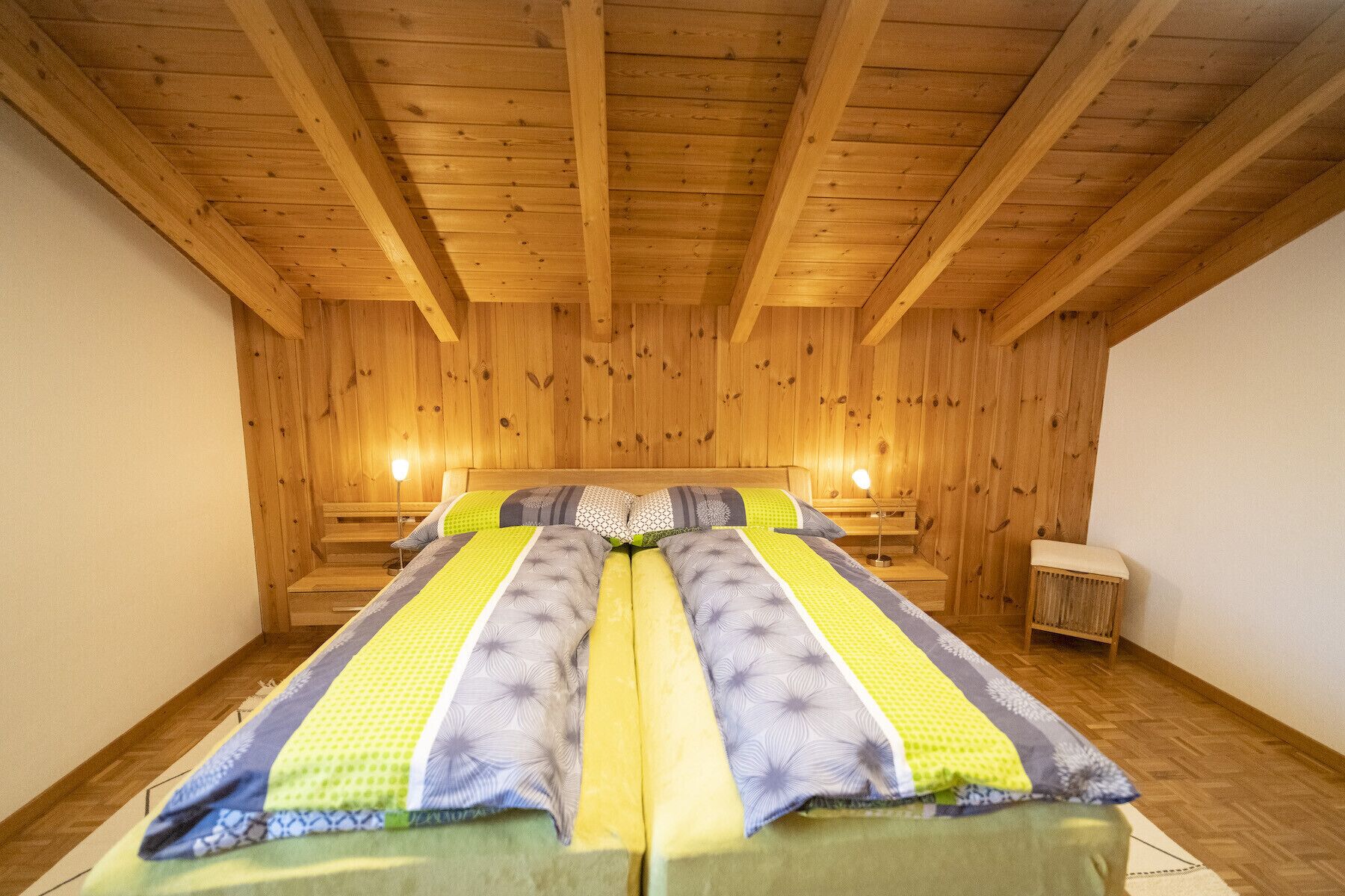 Una habitación con techo y paredes de madera, una cama con ropa de cama estampada y dos lámparas de noche.