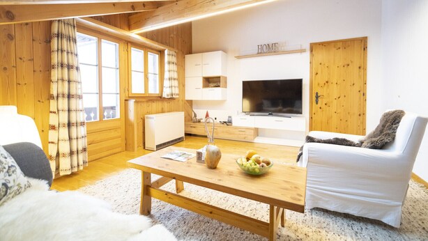 A cozy living room with wooden walls, a large TV, and a dining area with a table and chairs.