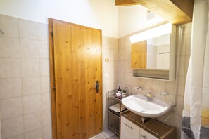 Une salle de bain avec une porte en bois, un lavabo blanc et un miroir.