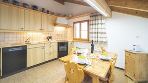 A kitchen with wooden cabinets, a tiled backsplash, a window with curtains, and a dining table set for two.