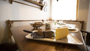 Une table en bois, sur laquelle se trouvent une assiette de fromage, un panier de pain et un couteau.