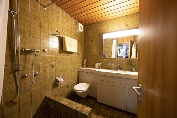 Een badkamer met douche, toilet, wastafel en kast.