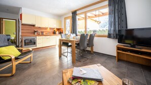 Ein modernes Wohnzimmer mit Essbereich, Küche und einem großen Fenster mit Vorhängen.