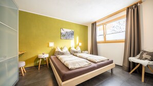 Ein modernes Schlafzimmer mit Bett, Nachttischen, einem Sessel und einem Fenster mit Vorhängen.