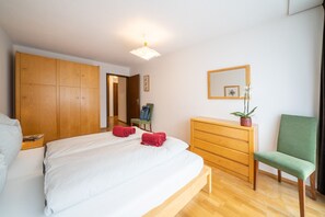 A bedroom with a bed, wooden wardrobe, a dresser, a chair, and a mirror. - Chasa La Plavna: Charming 2.5 room flat with large balcony near the golf course (Vulpera)