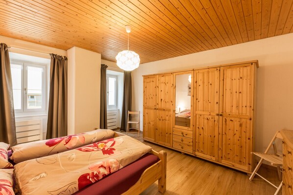 A bedroom with two beds, a wooden wardrobe, a desk, and a window with curtains.