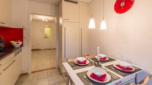 Moderni keittiö, jossa on valkoiset kaapit, punainen kello ja ruokailutila, jossa on neljälle katettu pöytä punaisine servetteineen ja valkoisine lautasiaan.