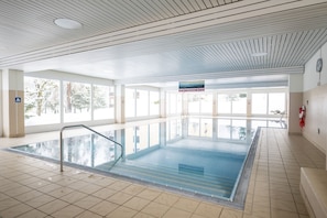 Een binnenzwembad met glazen wanden, betegelde vloer en een plafond met een regelmatige structuur.