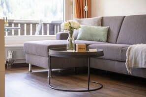 A modern living room with a grey sofa, a round coffee table with a vase of white flowers, and a wooden block labeled "Allegra".