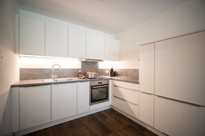 Una cocina moderna con armarios blancos, un lavamanos de acero inoxidable y un horno empotrado.