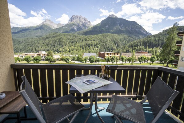 A balcony with a table and chairs, overlooking a mountainous landscape with buildings in the background.
