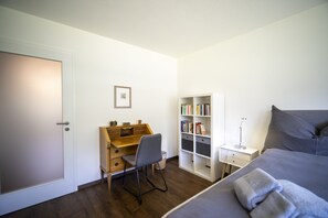 A bedroom with a bed, a desk, a chair, a bookshelf, and a bedside table. - Brentschpark No. 33: Charming renovated 2.5-room flat in the quiet located Brentschpark (Scuol)