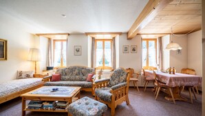 Ein gemütliches Zimmer mit einer Couch, Sesseln, einem Esstisch und einem Bücherregal.