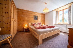 Una habitación acogedora de madera con una cama, una mesita de noche, una silla y una ventana con cortinas.