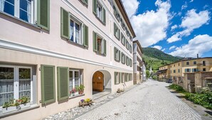 Eine Kopfsteinpflasterstraße gesäumt von traditionellen Gebäuden, mit Rundbogenportalen und grünen Fensterläden.