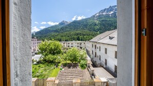 Blick aus einem Fenster auf einen Innenhof mit Gebäuden, einem Baum und einem Gebirge.