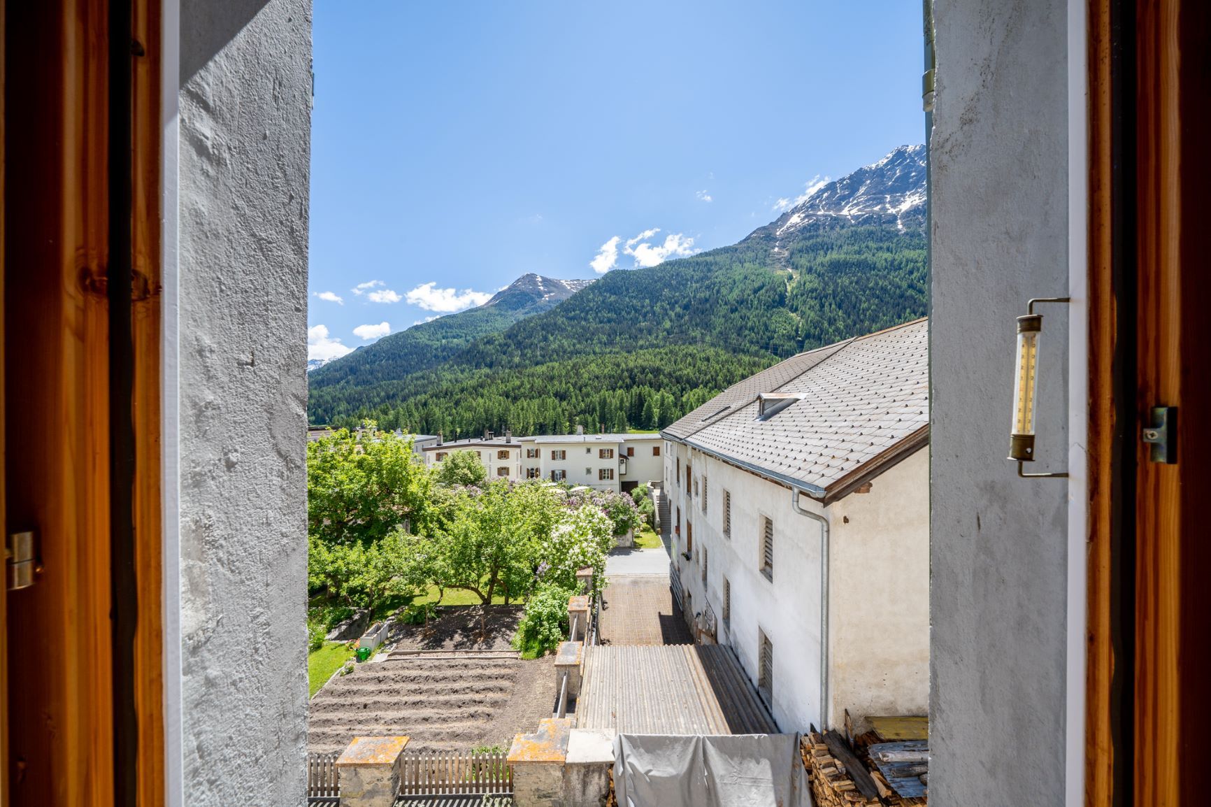 Vista desde un balcón sobre un pueblo con edificios y una cadena montañosa al fondo.