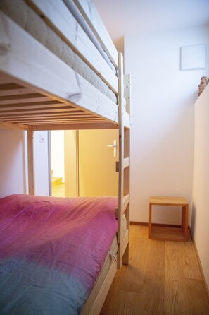 A bunk bed with a pink bedspread in a room with wooden flooring and a small wooden table. - CHasa Avant Muglins: Garden flat with a view (Scuol)
