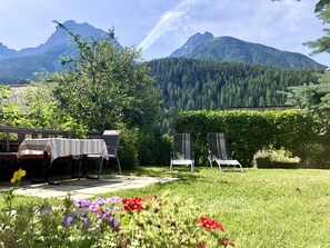 A garden with a table and chairs, a hedge, and a mountain view. - CHasa Avant Muglins: Garden flat with a view (Scuol)