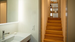 Un baño con un lavamanos blanco, un espejo y una escalera de madera que lleva a una plataforma con estanterías.