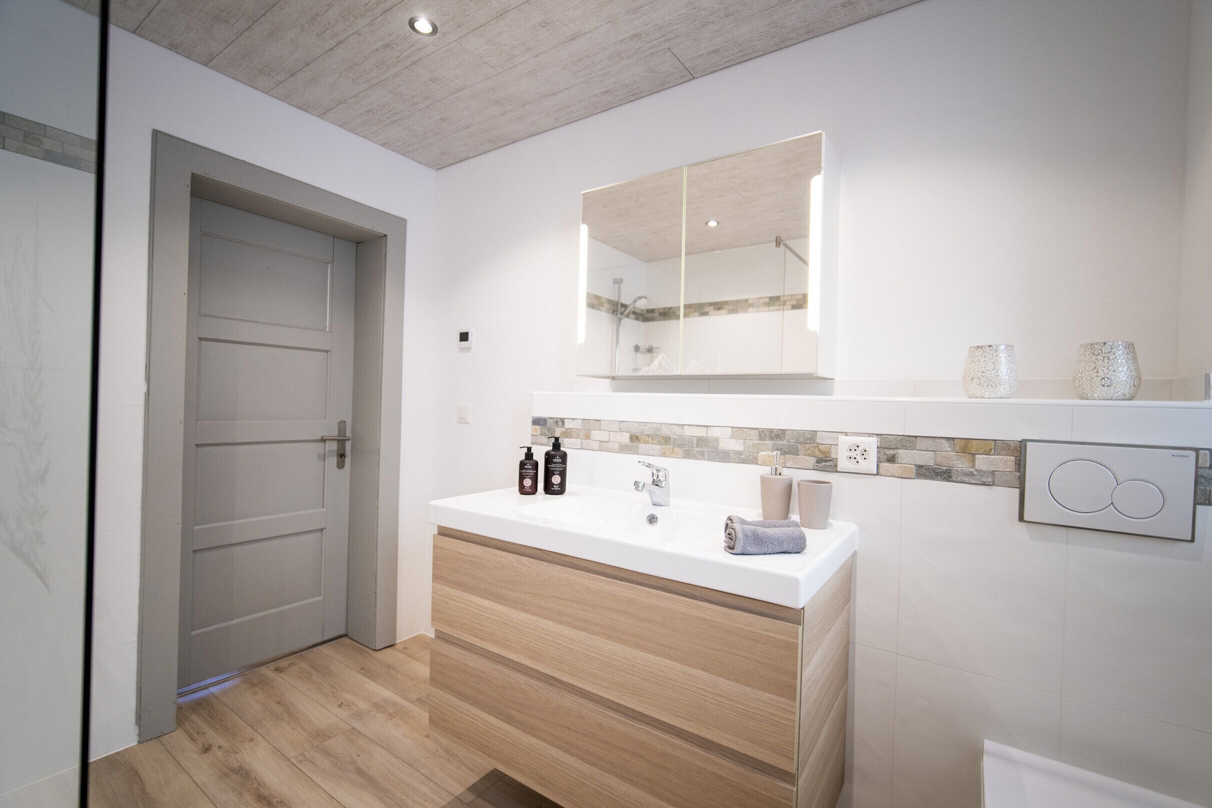 A modern bathroom with a wooden vanity, a large mirror, and a tiled backsplash.