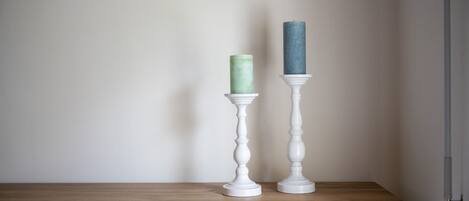Deux chandeliers blancs, chacun contenant une bougie, sont posés sur une étagère en bois devant un mur uni.