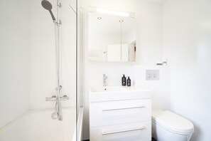 Ein modernes Badezimmer mit Duschkabine aus Glas, einem weißen Waschbecken mit Spiegel darüber und einer Toilette.