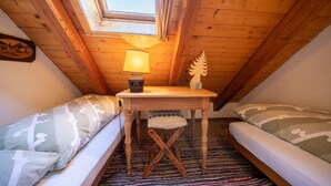 Une chambre mansardée chaleureuse avec un plafond en bois, une petite table avec une lampe et deux lits dotés d’oreillers à motifs.