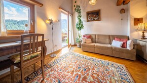 Un salon chaleureux avec une table à manger en bois, un canapé, un tapis à motifs et une plante suspendue.