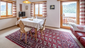 Ein Essbereich mit Tisch für zwei Personen, einem Fernseher und Blick auf eine gebirgige Landschaft durch große Fenster.