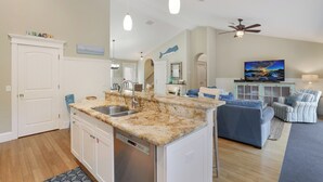Una cucina moderna con piani in granito, lavastoviglie e zona pranzo con divano blu e poltrone a righe.