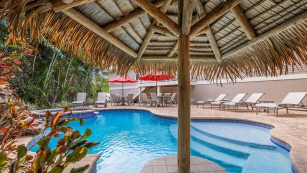 Una piscina con tetto di paglia e poltrone relax.