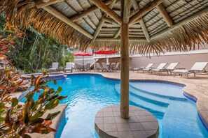 Una piscina con techo de paja y sillas de descanso.