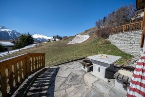 Eine Steinterrasse mit Tisch und Bank, mit Blick auf einen verschneiten Berg und eine Steinmauer.