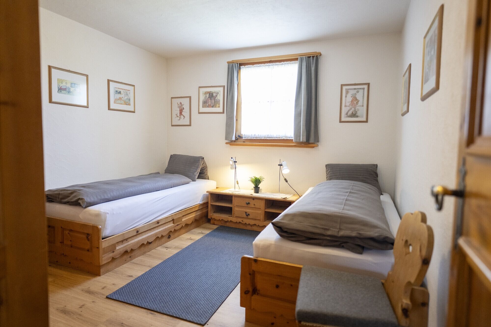 A bedroom with two wooden bunk beds, a desk with a lamp, and framed pictures on the wall.