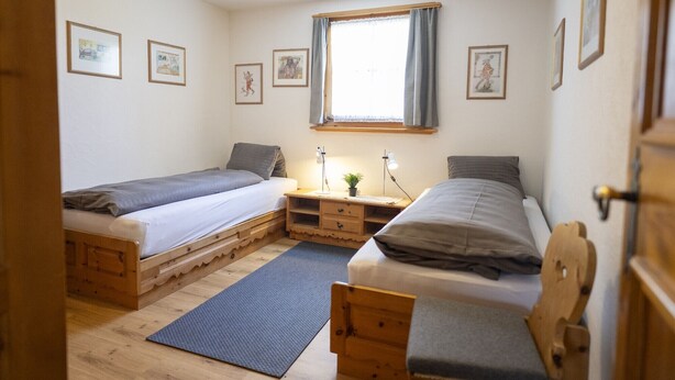 A bedroom with two wooden bunk beds, a desk with a lamp, and framed pictures on the wall.
