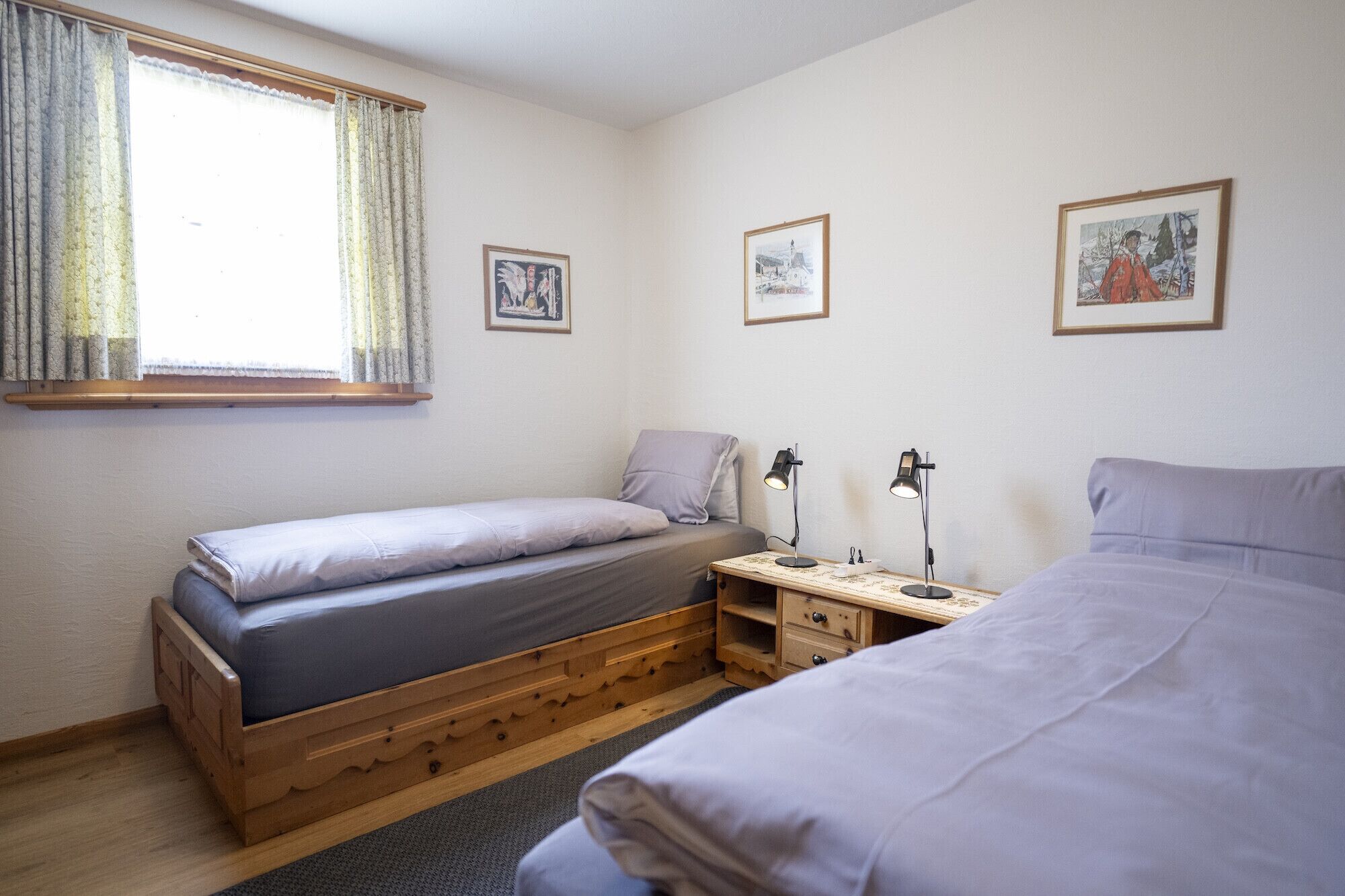A bedroom with two single beds, a window with curtains, and two bedside tables with lamps.