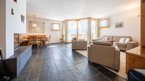 A spacious living area with a dining table, sofas, and a large window with curtains.
