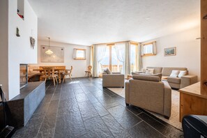 A spacious living area with a dining table, sofas, and a large window with curtains.