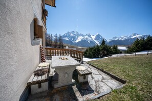 Un banco de piedra con una mesa y una barandilla de madera con vistas a un paisaje montañoso nevado.