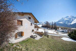 Ein zweistöckiges Gebäude mit Balkon, umgeben von verschneiter Landschaft und Bergen im Hintergrund.