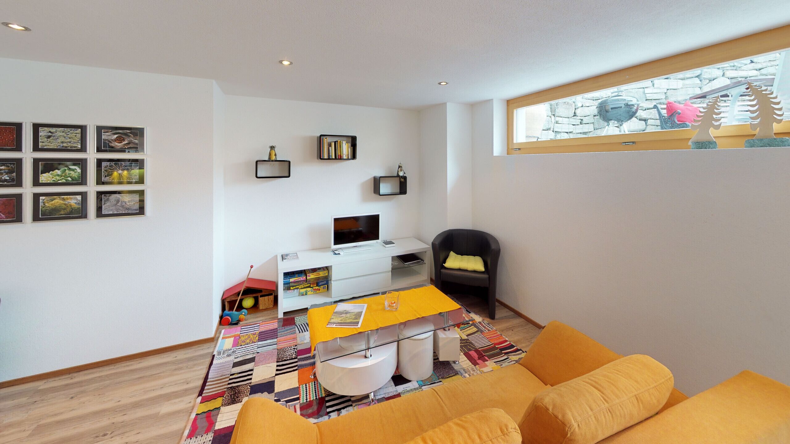A modern living room with a sofa, a TV, a desk with a computer, and a bookshelf.