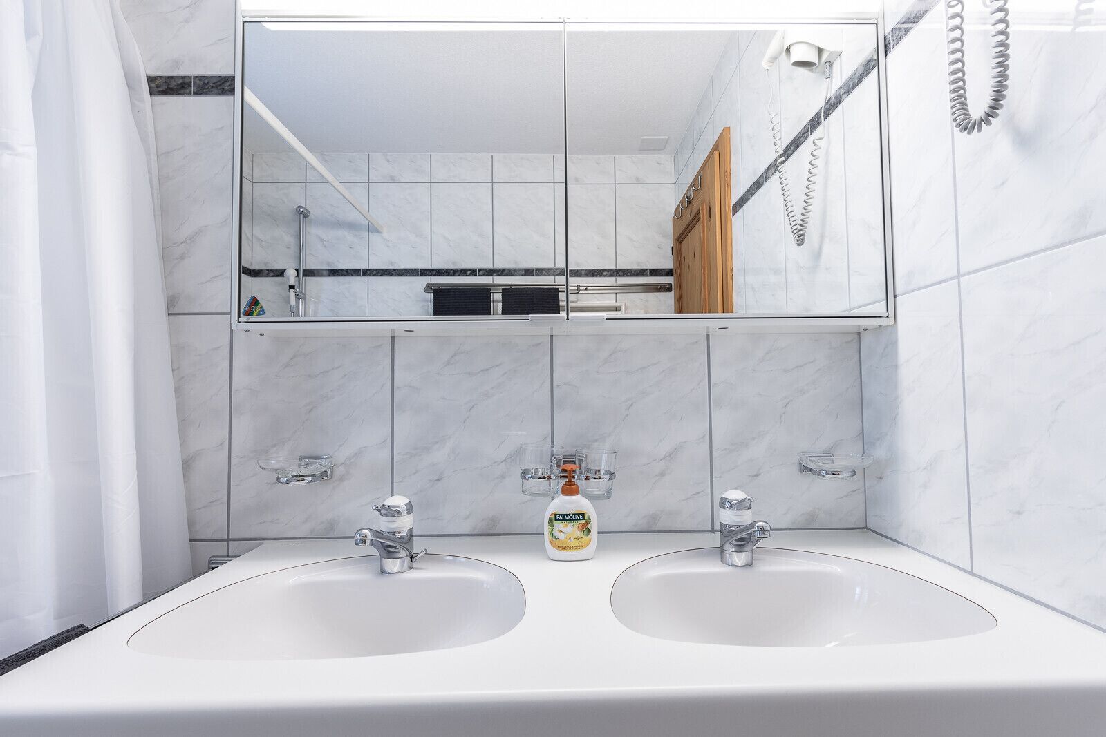 A bathroom with two sinks, a mirror, and a shower.